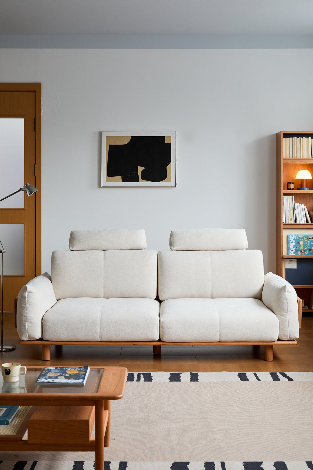 White 2 seater sofa in a living room with a bookshelf and abstract art on the wall.