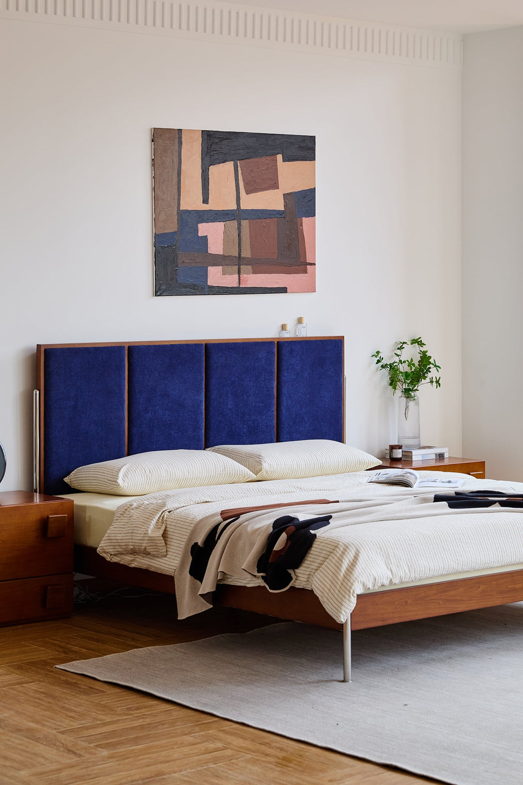 Bedroom with a blue upholstered headboard and abstract painting on the wall.