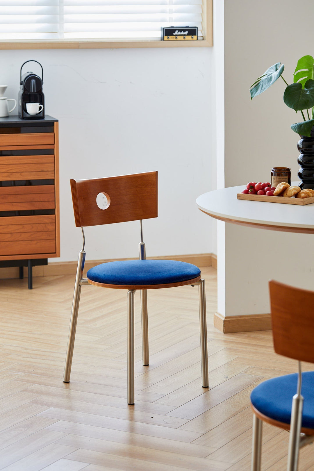 Bauhaus-style dining chair with blue velvet seat and wood backrest featuring circular cutout, paired with minimalist table in a modern breakfast nook.