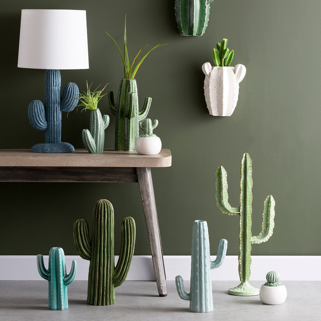 Assorted ceramic cactus plants and lamp, beautifully displayed against a green wall for a modern and playful decor theme.
