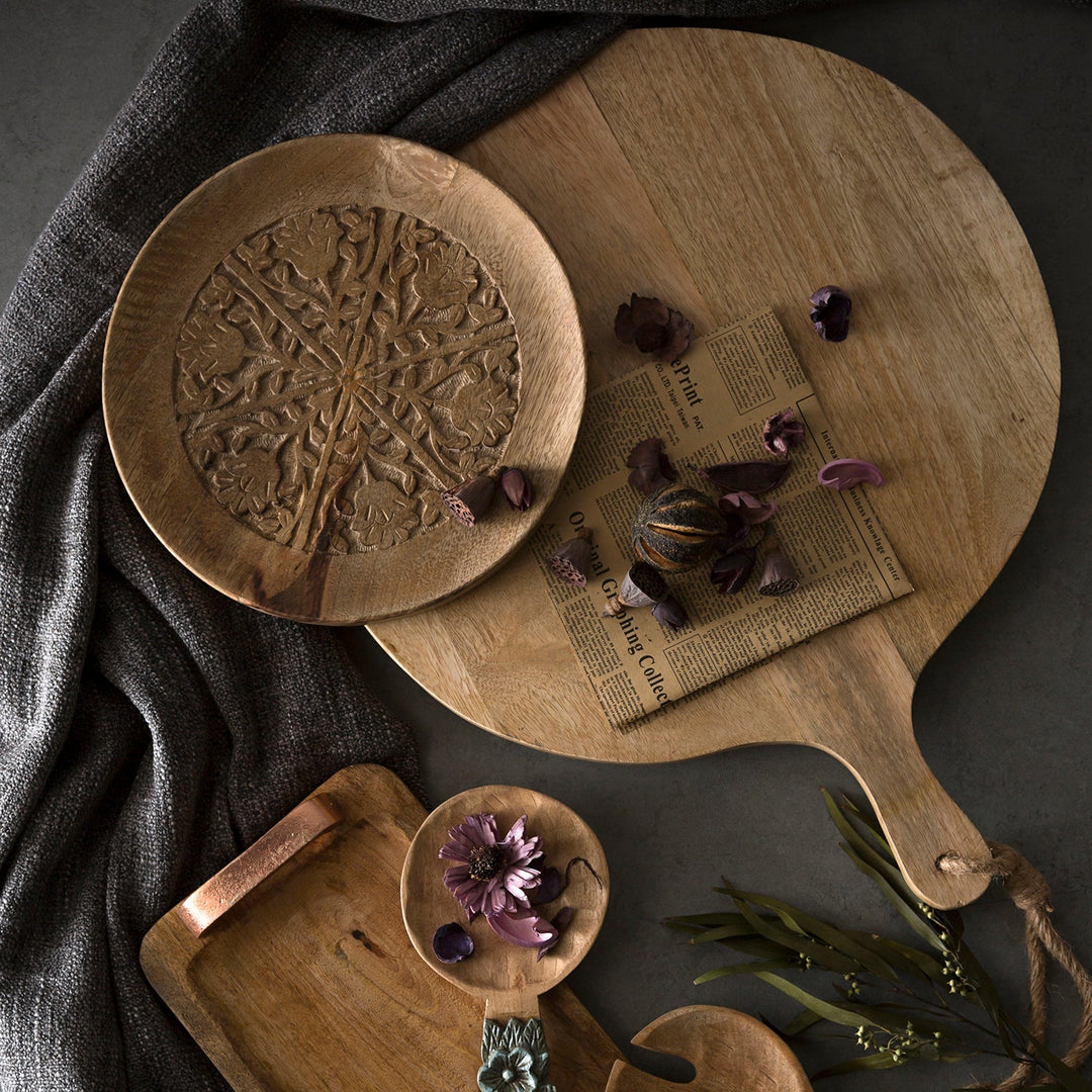 Rustic wooden serving platters and decorative plates with intricate carvings, arranged with dried flowers for a vintage aesthetic.