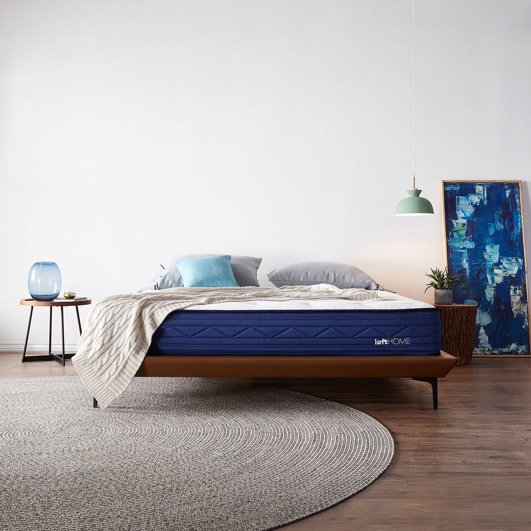 Loft Home premium mattress collection, featuring a navy blue mattress on a modern wooden bed frame, complemented by cozy pillows and a knitted throw, perfect for a restful and stylish bedroom.