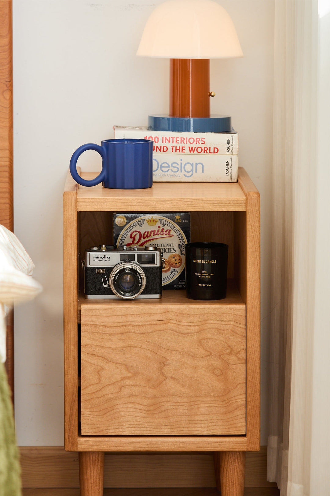 Wooden nightstand with books, a mug, a camera, and a plate on top