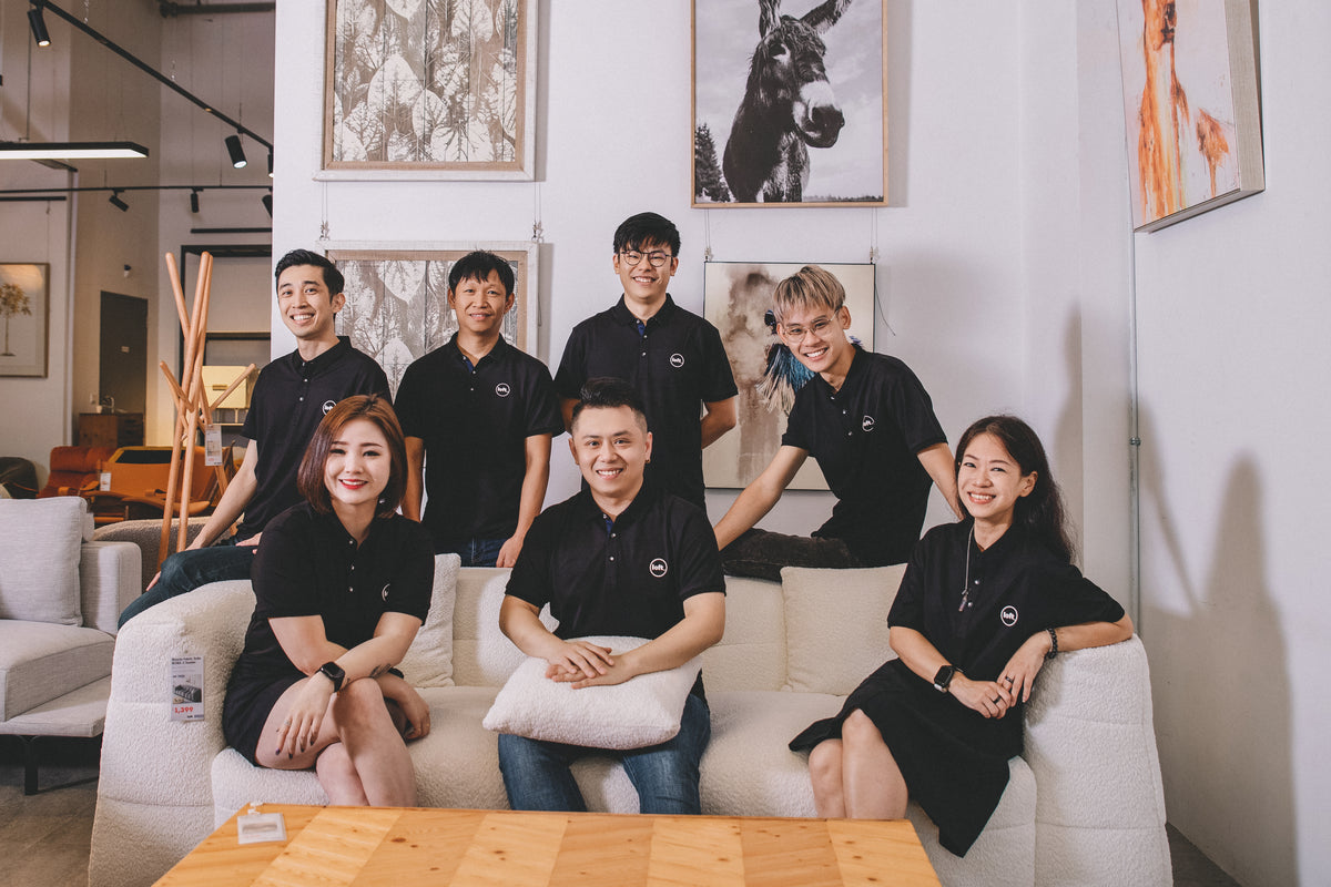 Group of people in matching black shirts sitting on a couch in a modern office setting.